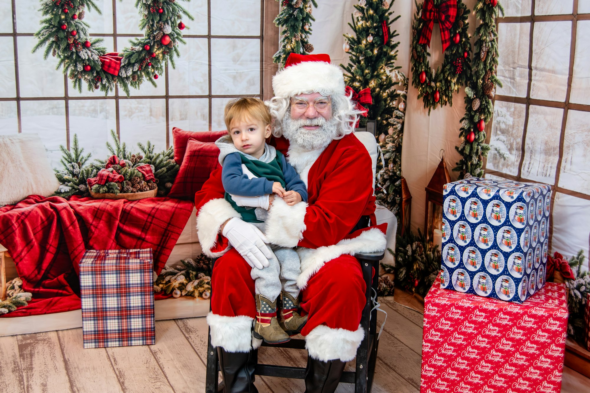 A child sits on Santa's lap, surrounded by festive decorations and wrapped gifts in a cozy holiday setting.