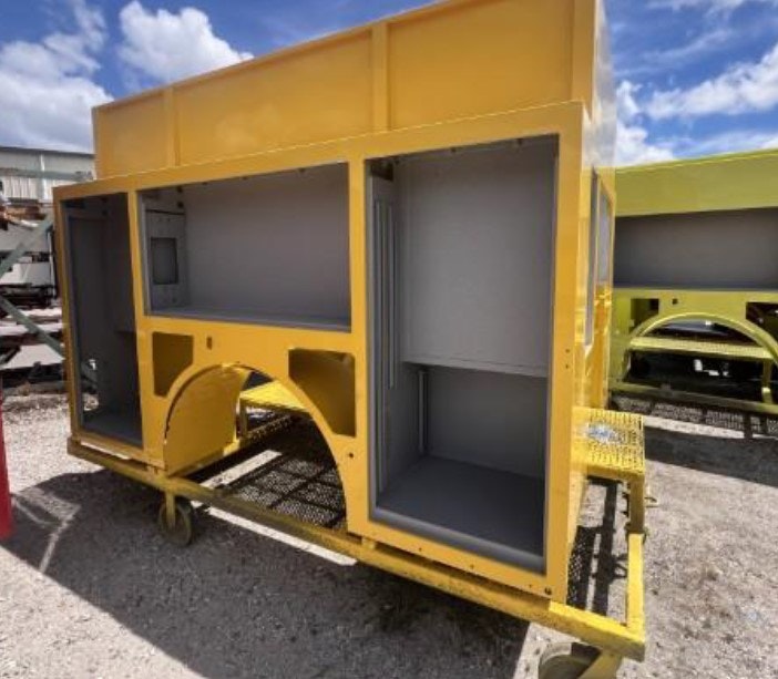 A large yellow metal structure with compartments on wheels outdoors.