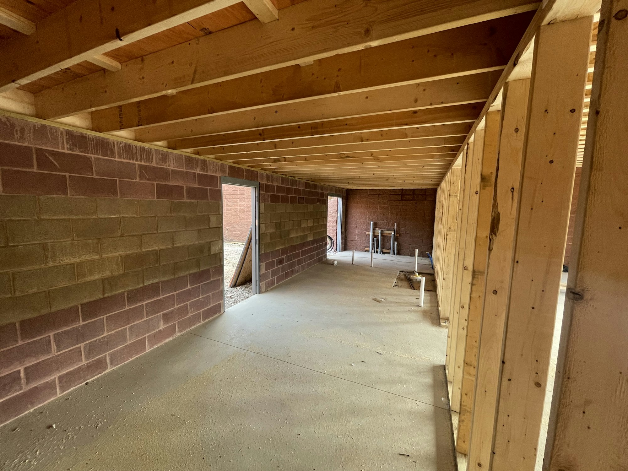 An unfinished interior space with brick walls, wooden rafters, and a concrete floor.