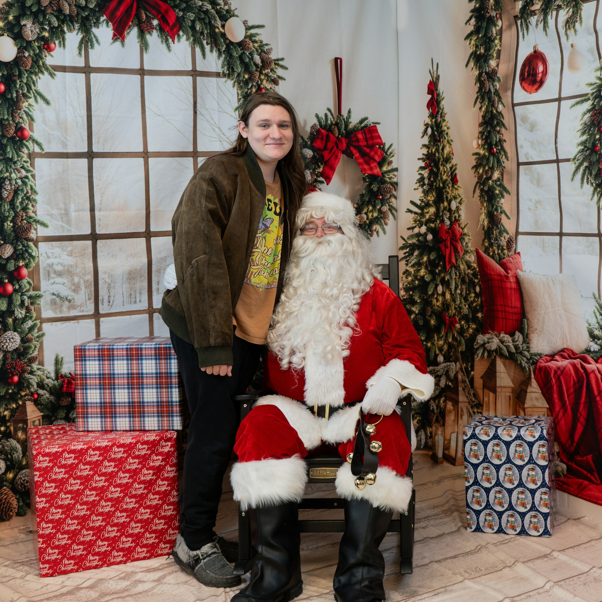 A person standing next to Santa Claus in a festive holiday setting with wrapped gifts and decorations.
