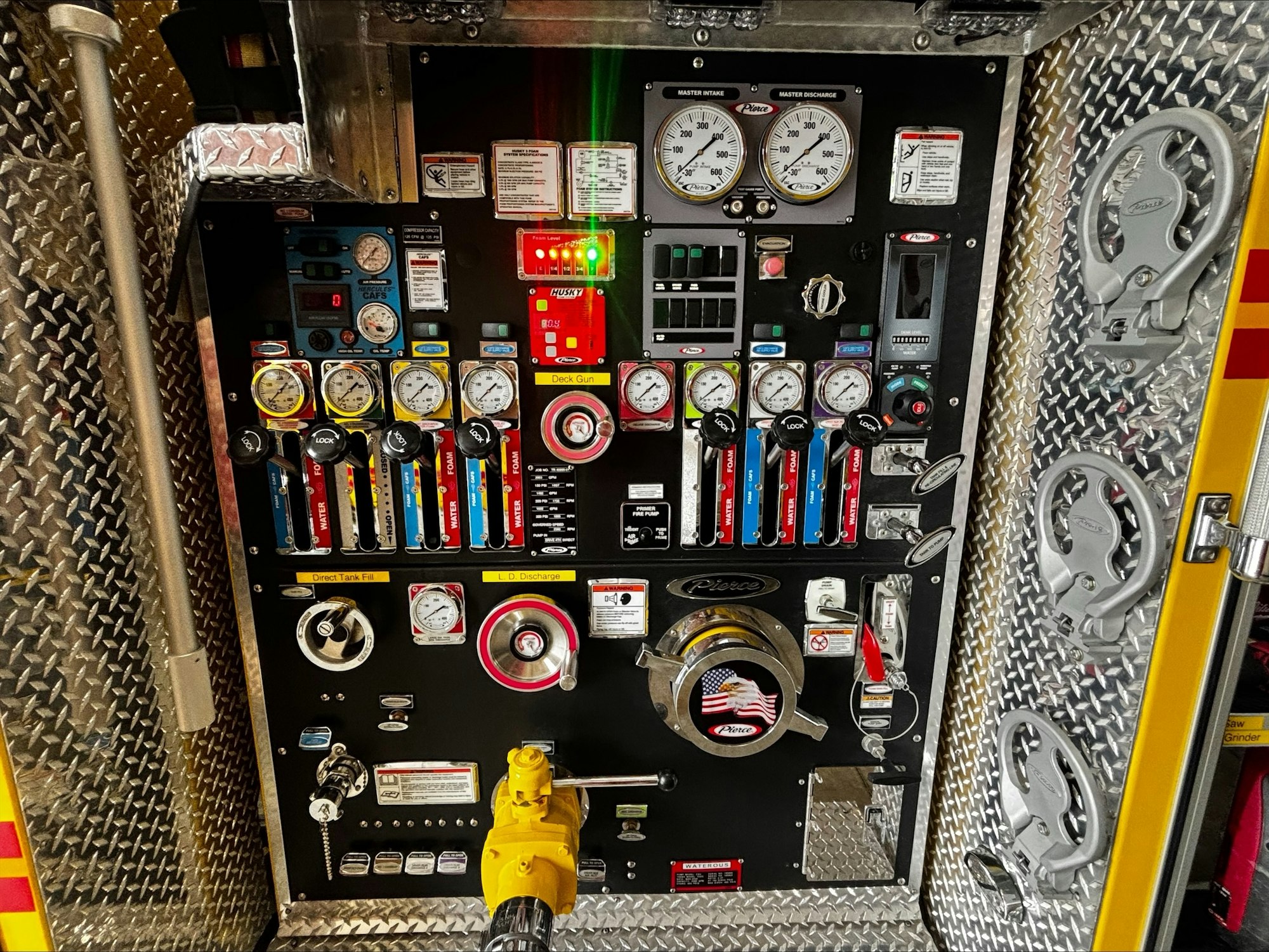The image shows a control panel from a fire truck, featuring gauges, valves, and controls for managing water pressure and discharge.