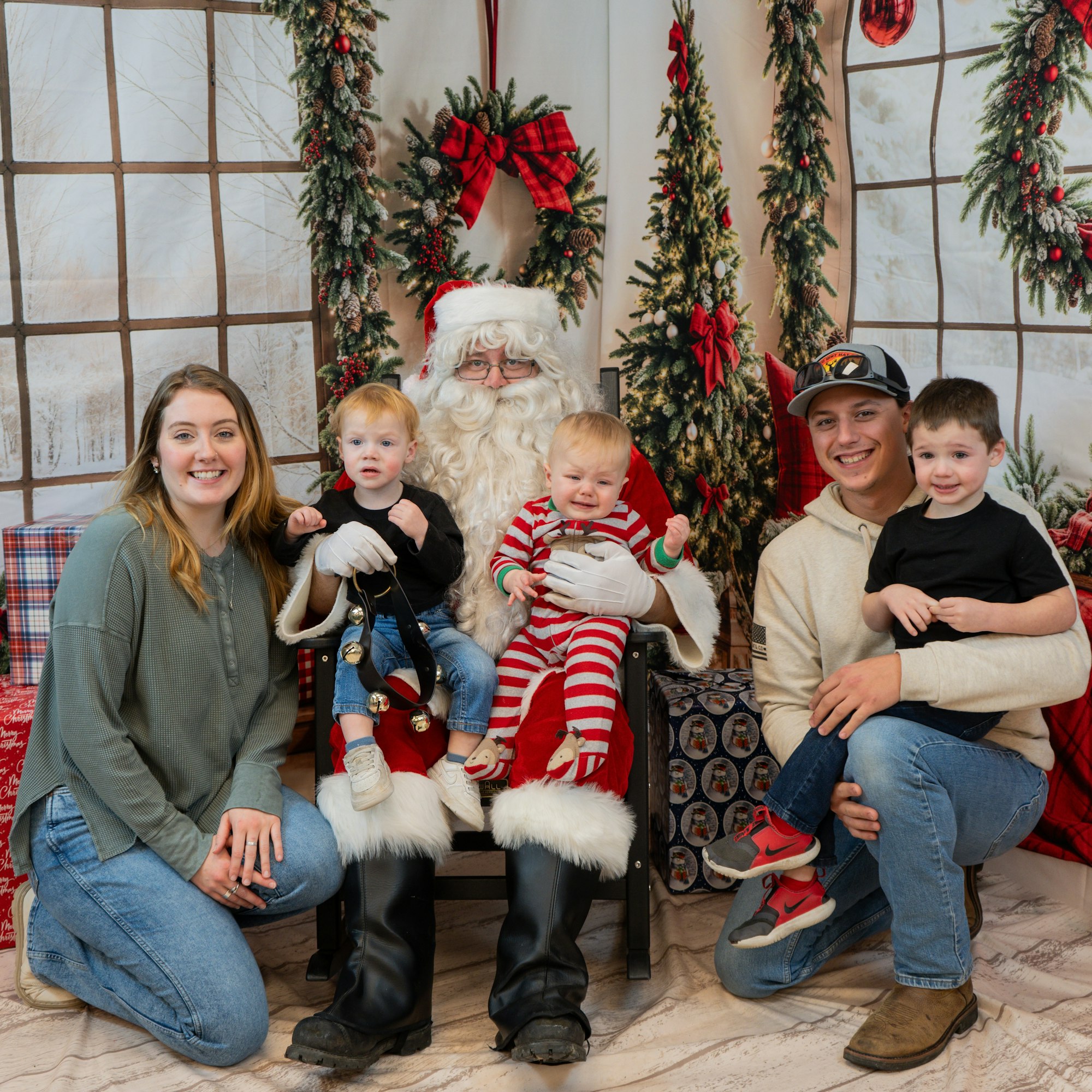 A family poses with Santa Claus in a festive setting, surrounded by holiday decorations and wreaths.