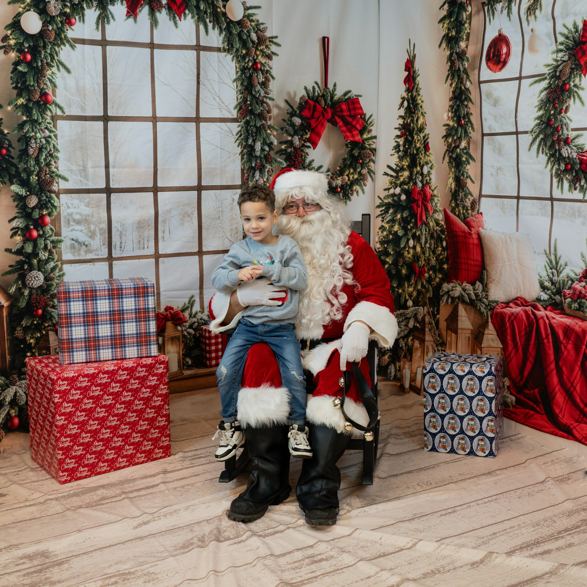 A child sits on Santa's lap in a festive setting with Christmas decorations and wrapped gifts.