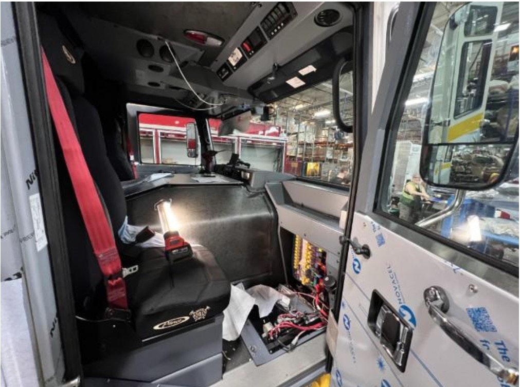Interior of a vehicle’s cockpit with a red seatbelt, control panel, wires, and a work light, possibly under assembly or maintenance.