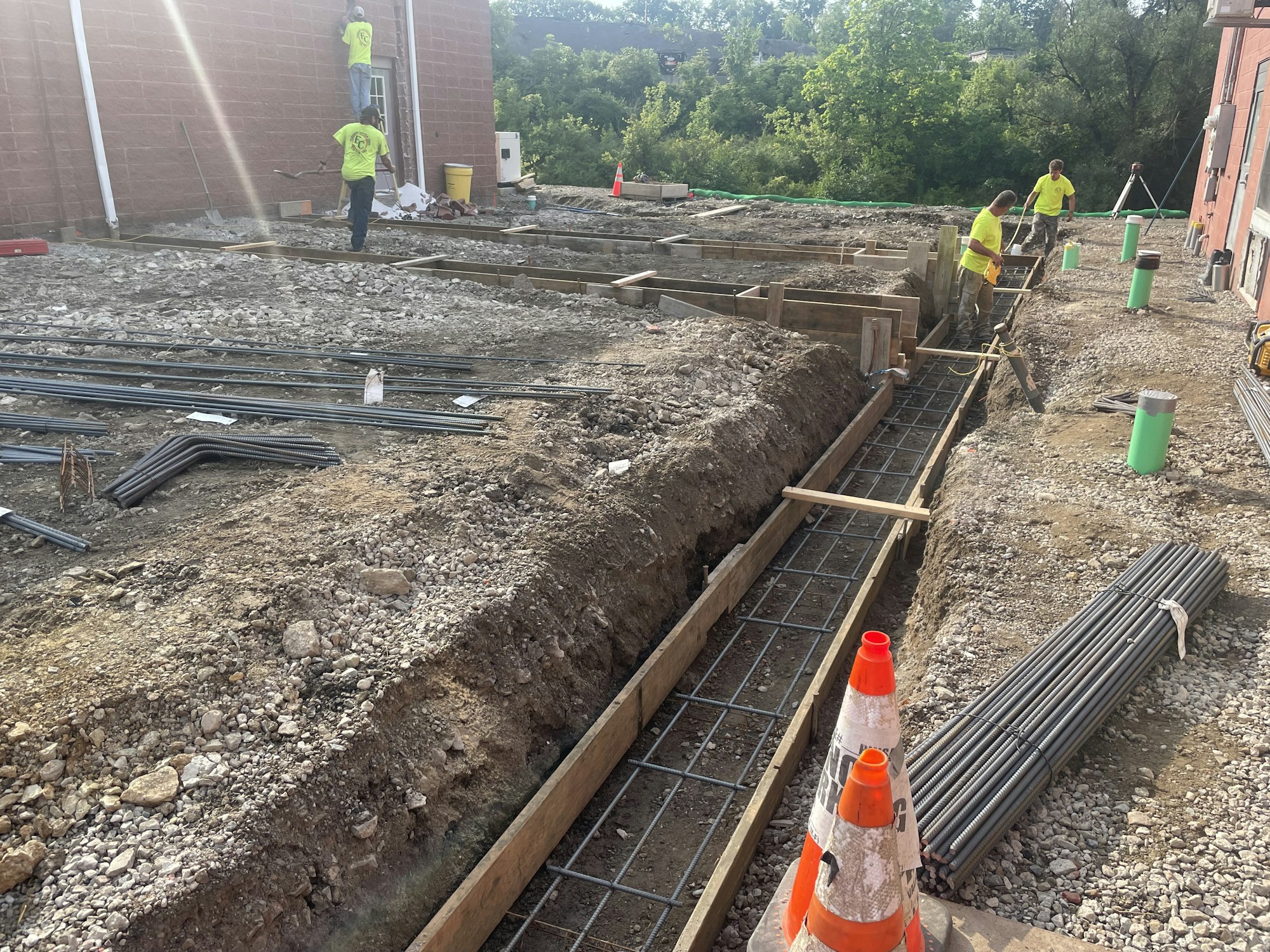 Construction site with workers, dug trenches, wooden forms, rebar, and safety cones.