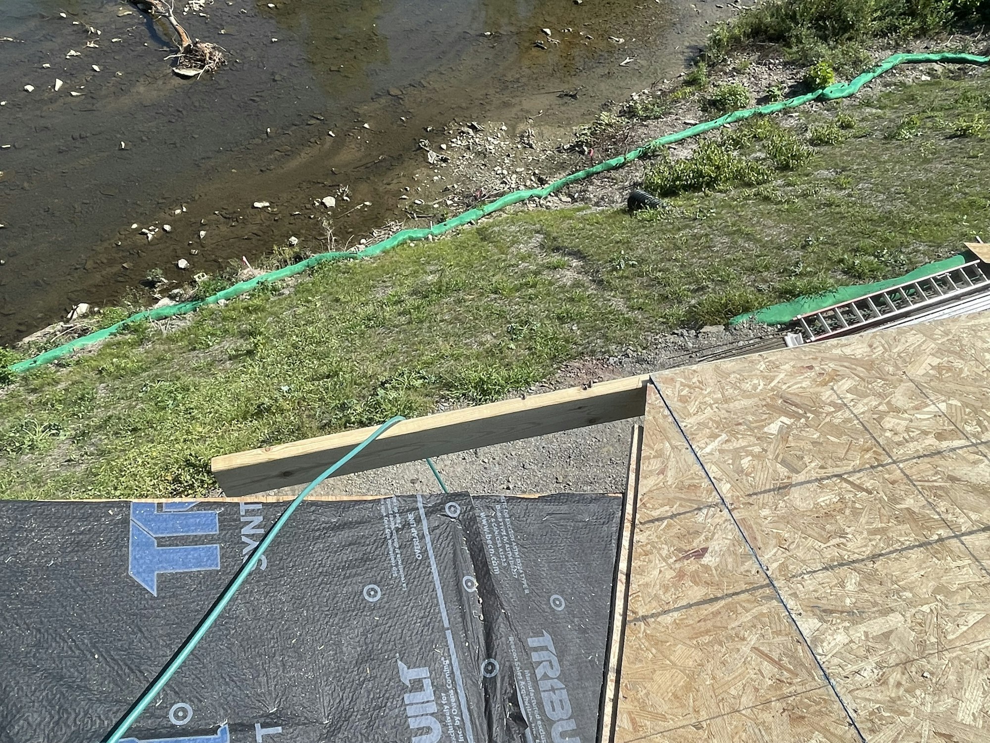 Construction site with wooden beams and waterproofing over riverbank view.