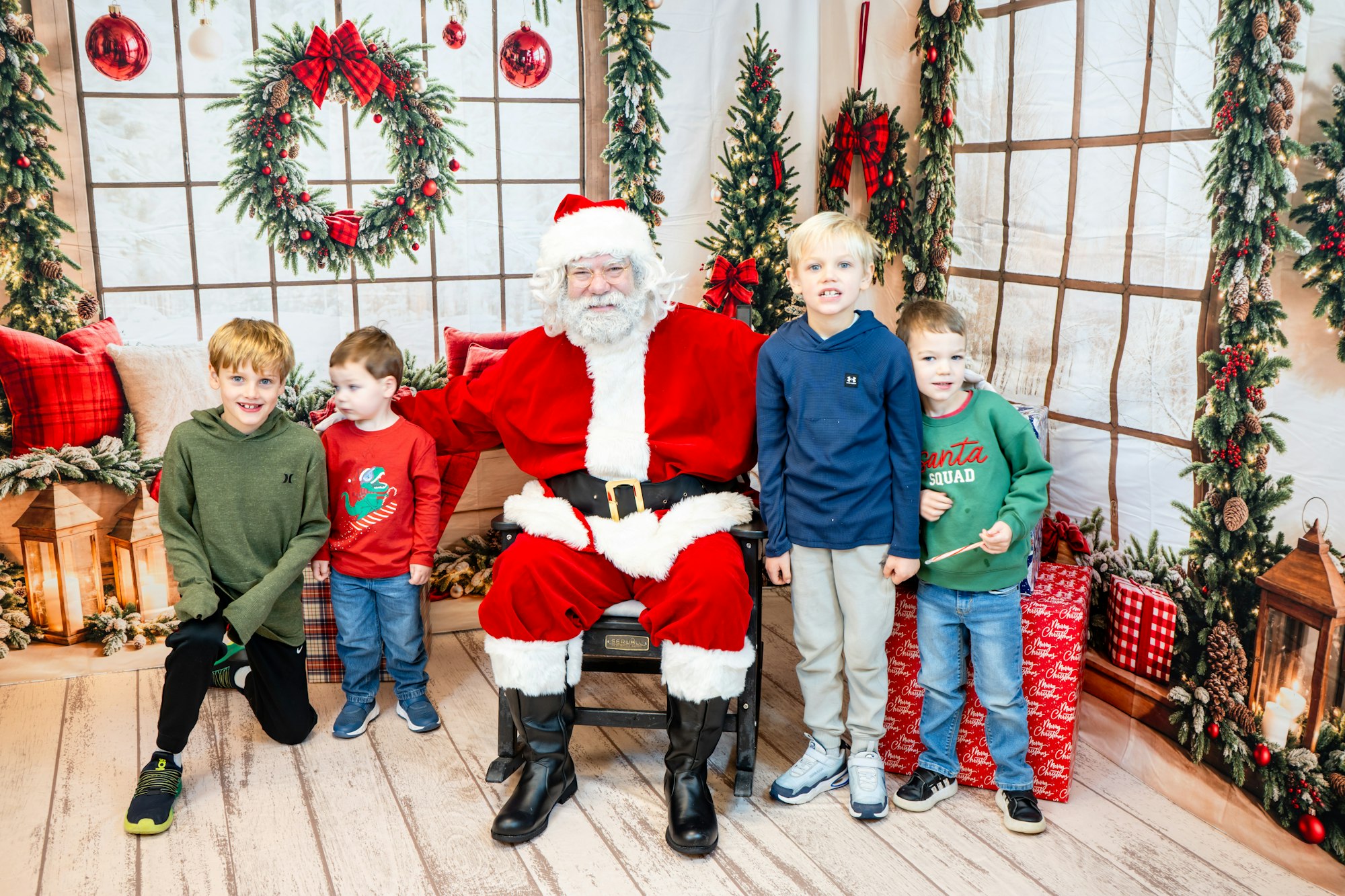 A group of four kids pose with Santa Claus in a festive holiday setting adorned with decorations and presents.