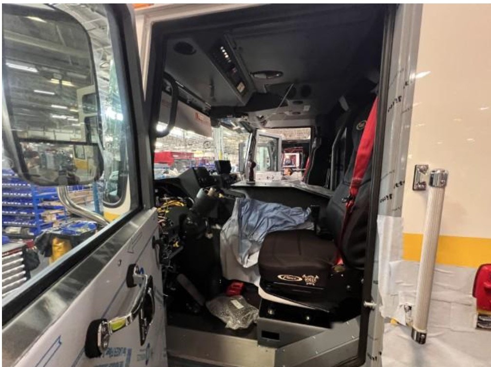 Interior view of a truck cab in a factory setting, showing a steering wheel, seats, and dashboard.