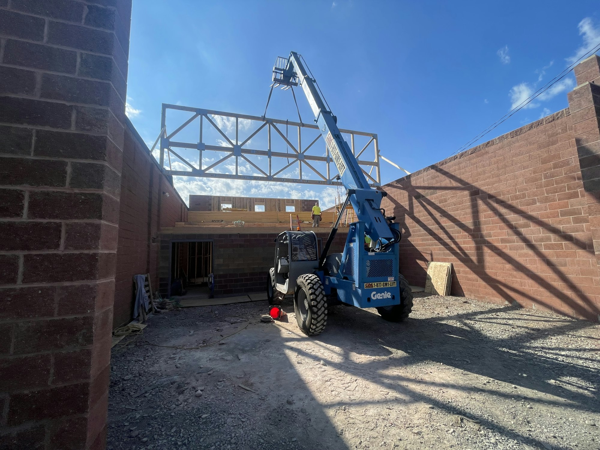 Telescopic handler and truss framework at a construction site with clear skies.