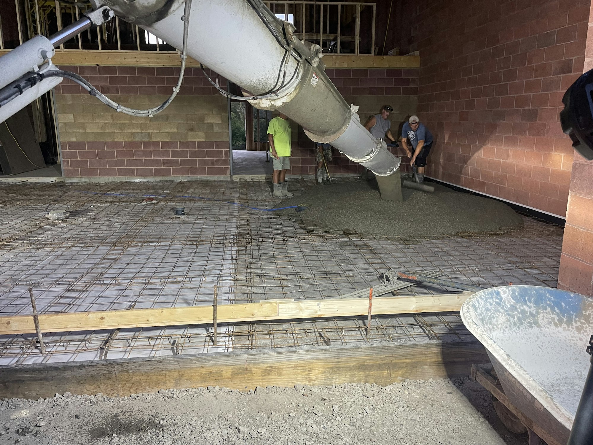 Concrete being poured by workers at a construction site with a cement mixer chute and metal reinforcement grid visible.