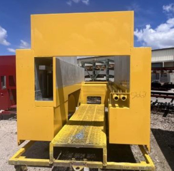Yellow industrial structure with open sections, possibly part of a larger machine or equipment, on a gravel surface.