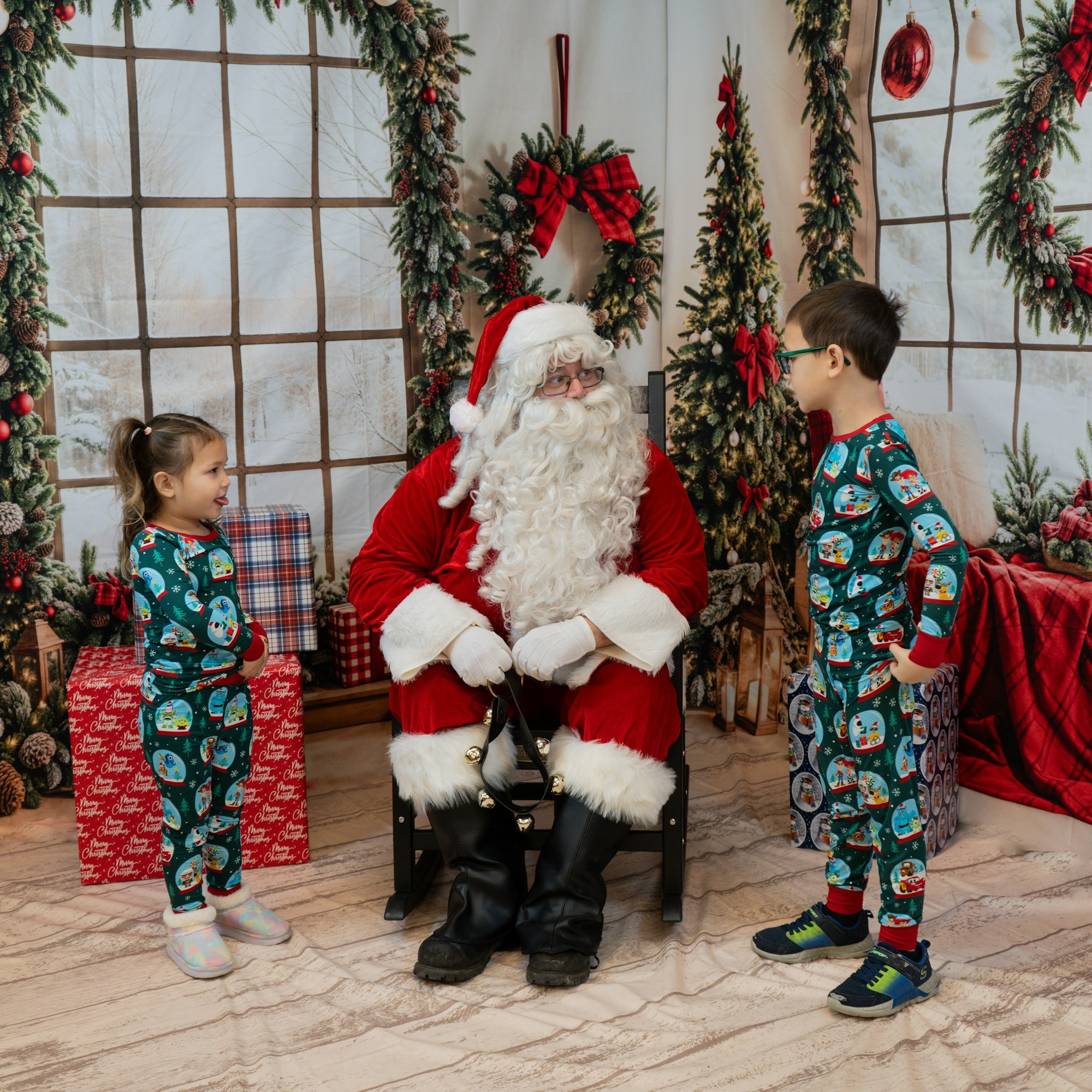 Santa Claus with two kids in festive pajamas, in a holiday-themed room with Christmas decorations and gifts.