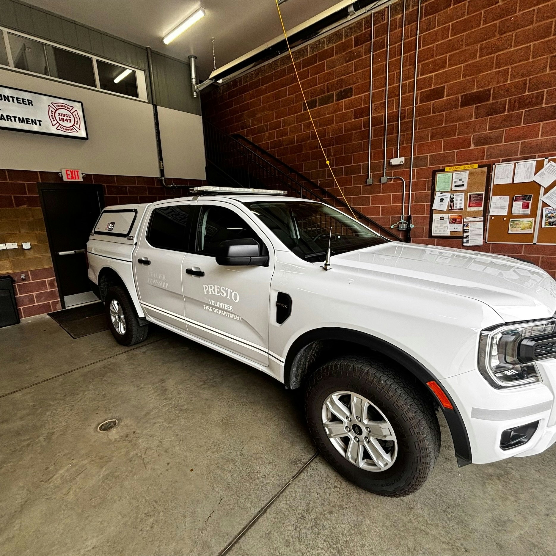 A white pickup truck is parked in a fire department garage, labeled for the Presto Volunteer Fire Department.
