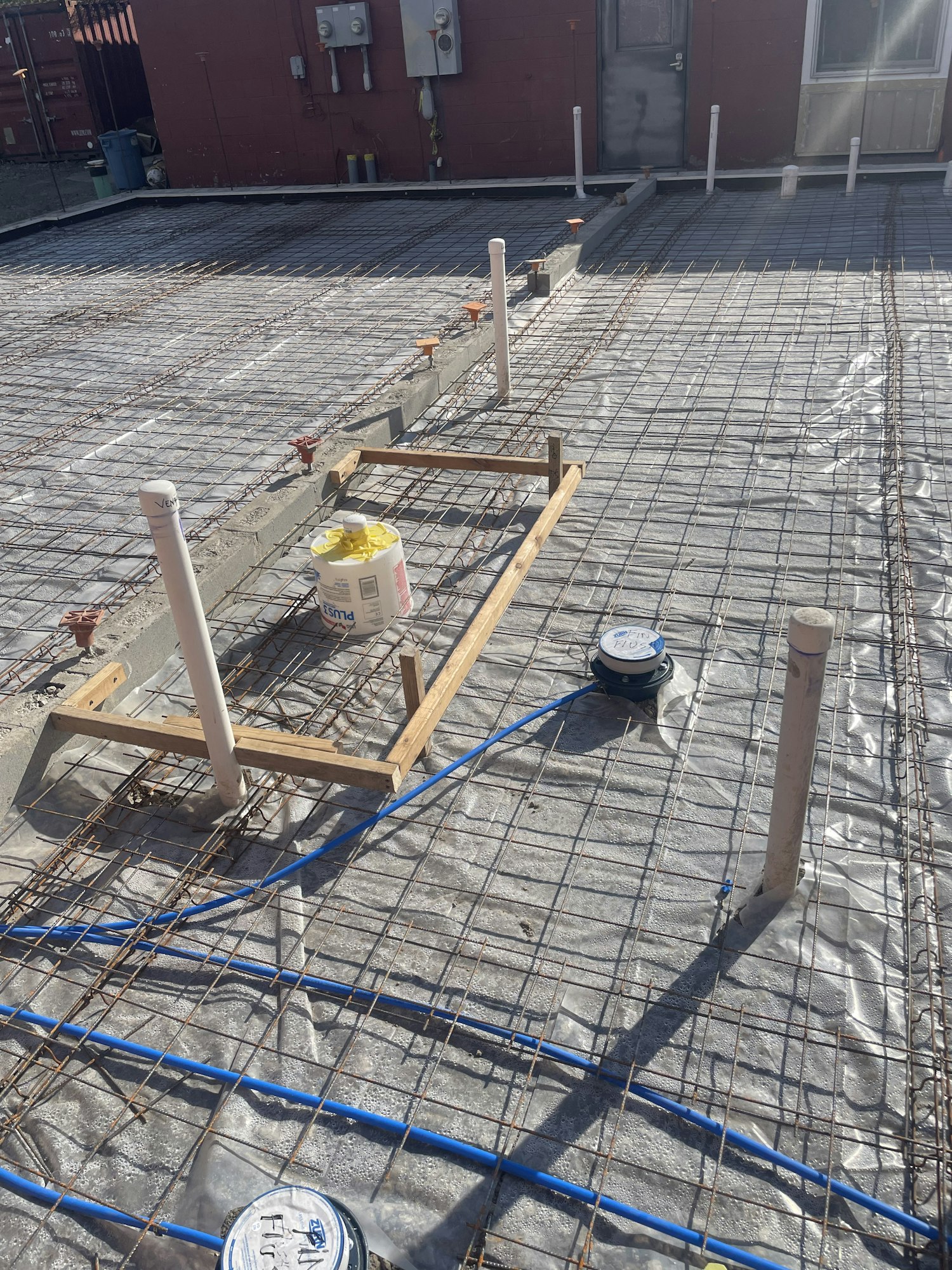 Scaffolding with a protective plastic sheet, wooden planks, electrical conduit, and construction materials against a building.