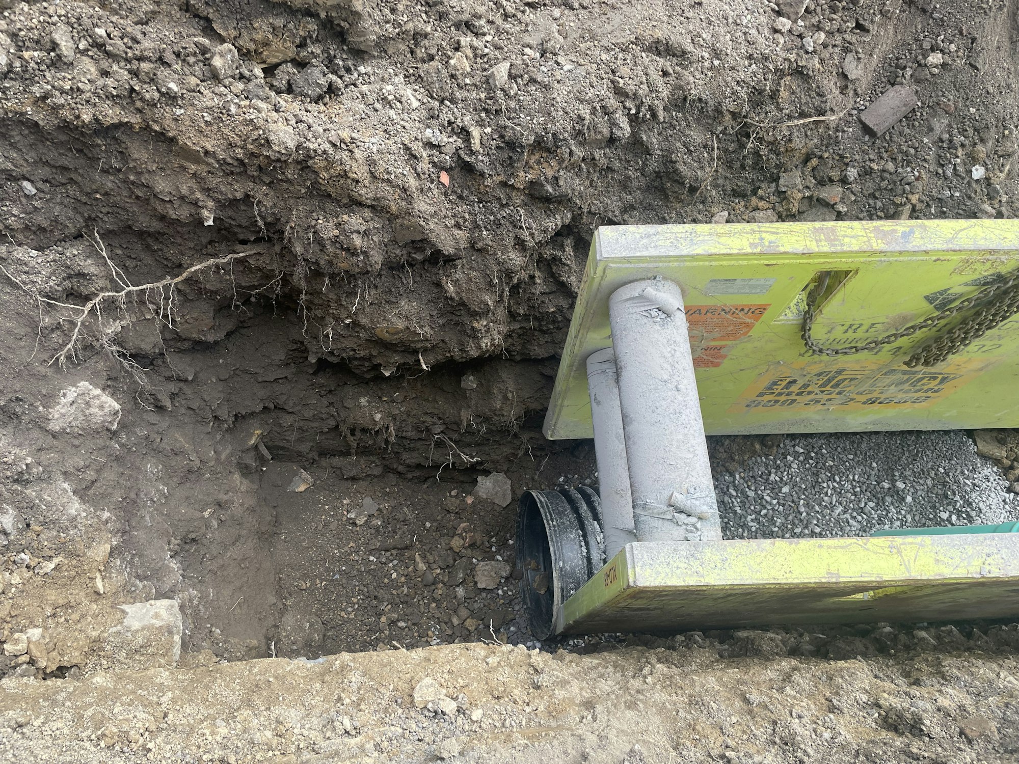Construction site with exposed drainage pipe, dirt, and safety barriers.
