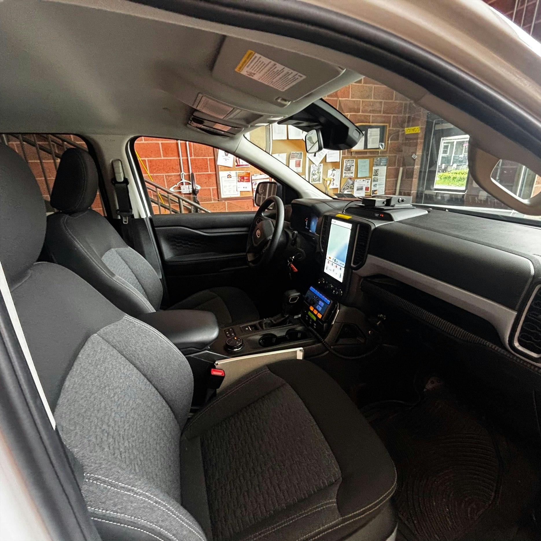 The image shows the interior of a vehicle, featuring black seats, a touchscreen display, and a dashboard with controls.