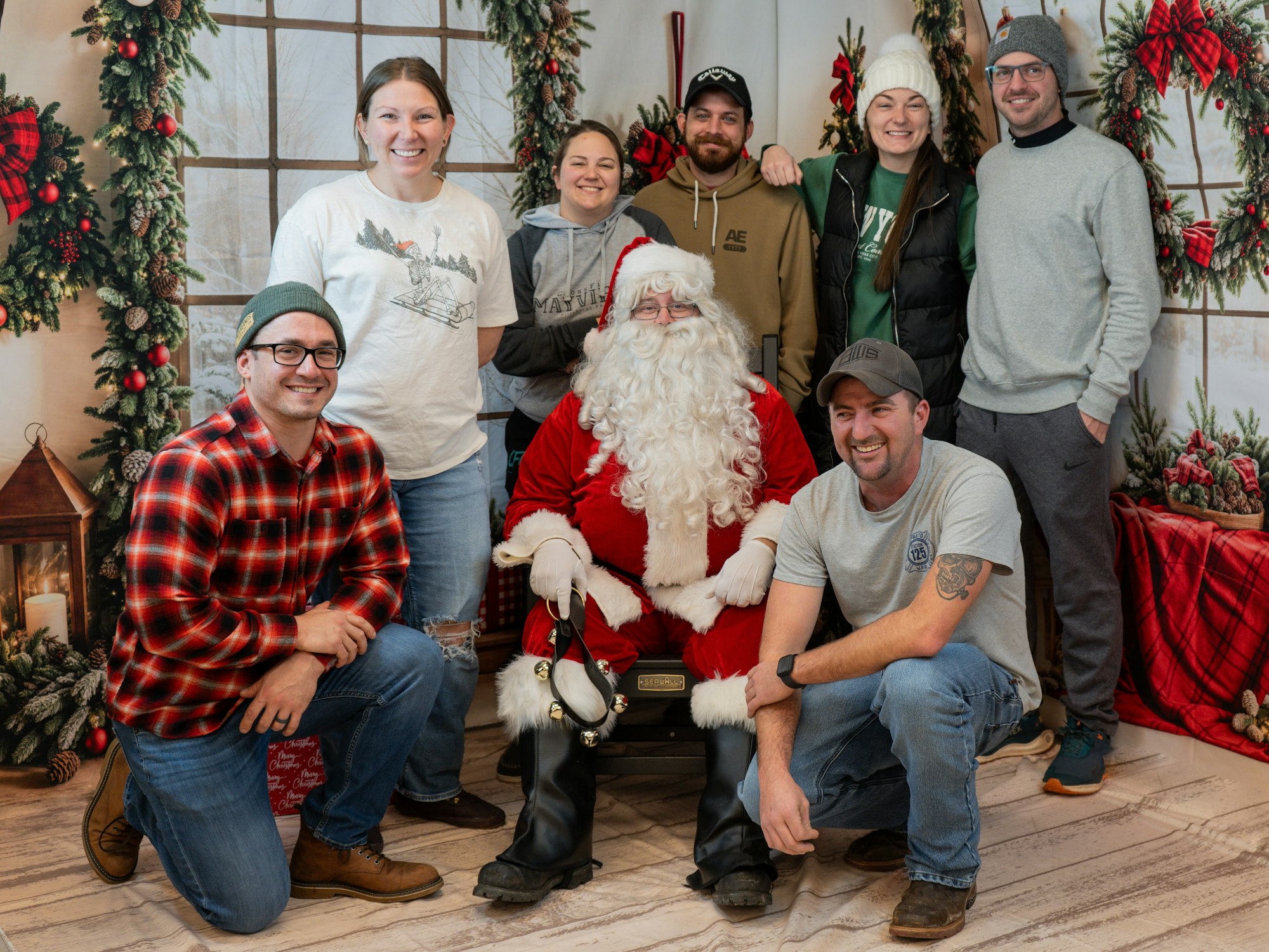 A group of people posing with Santa Claus in a festive holiday setting with wreaths and garlands.