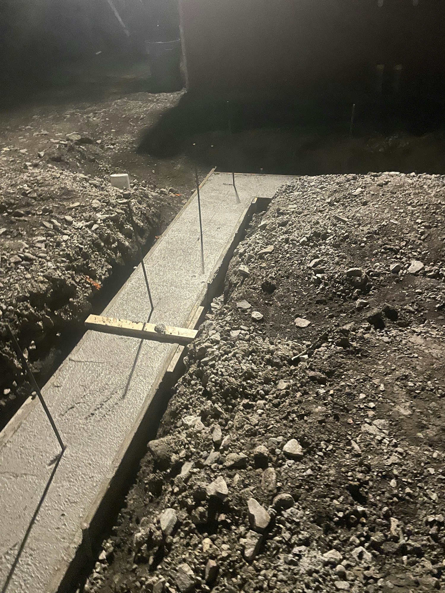 Asphalt and concrete surface with some debris, probably a roadside or pavement, taken at night.
