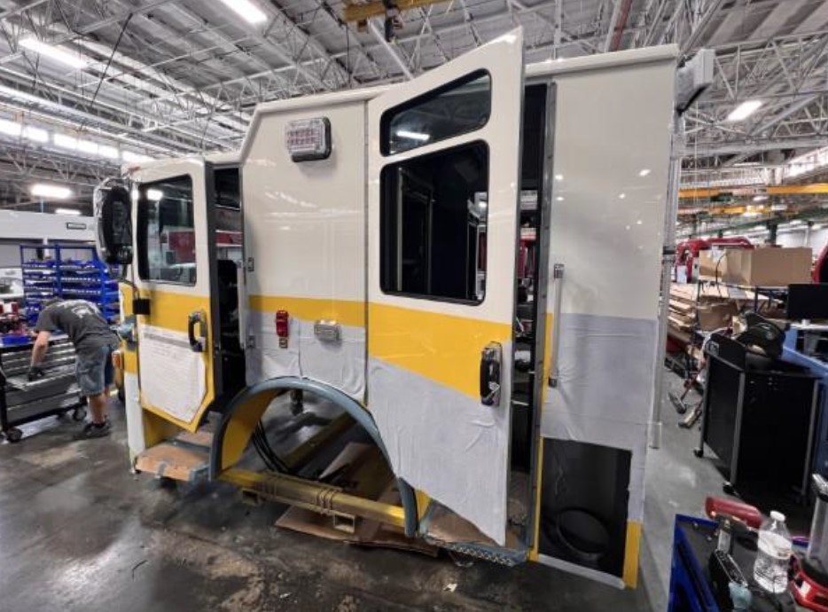 A partially assembled emergency vehicle, possibly a fire truck, in a workshop with a person working nearby.