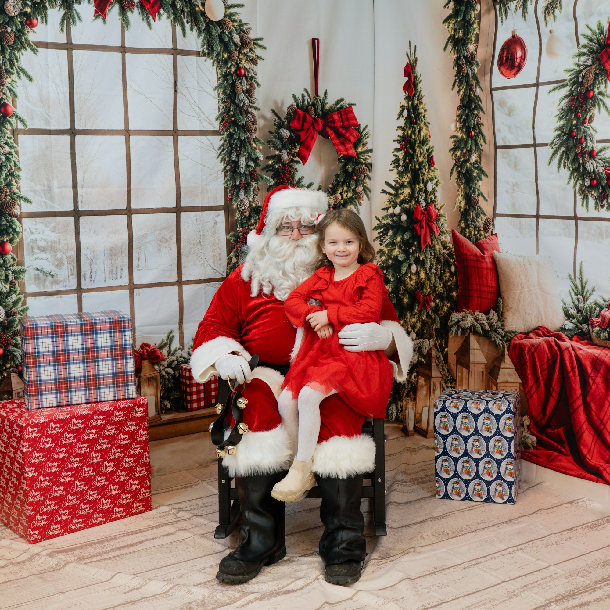 Santa Claus and a child in red sitting together, surrounded by Christmas decorations and gifts.