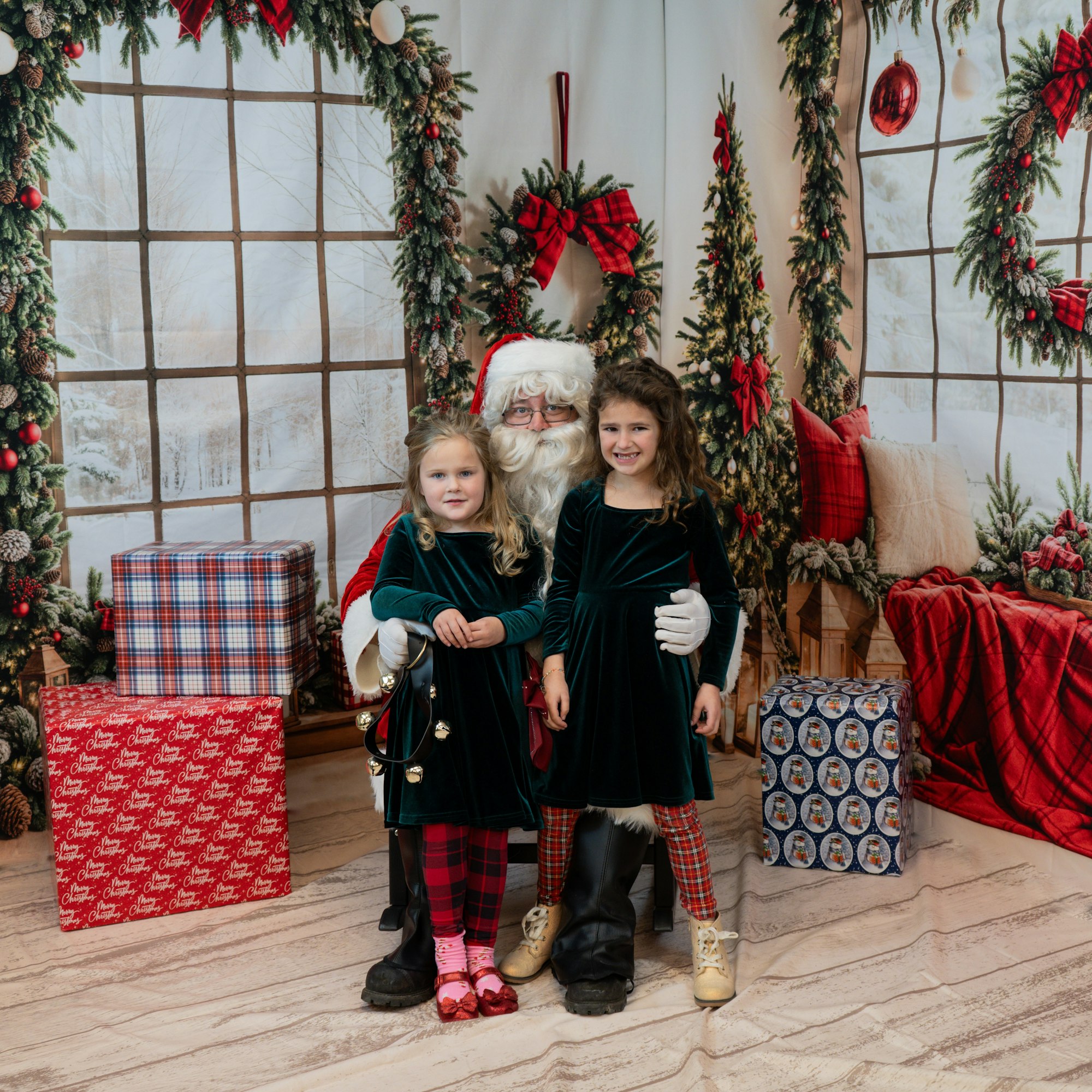 Two children standing with Santa Claus in a festive room with Christmas decorations and wrapped gifts.