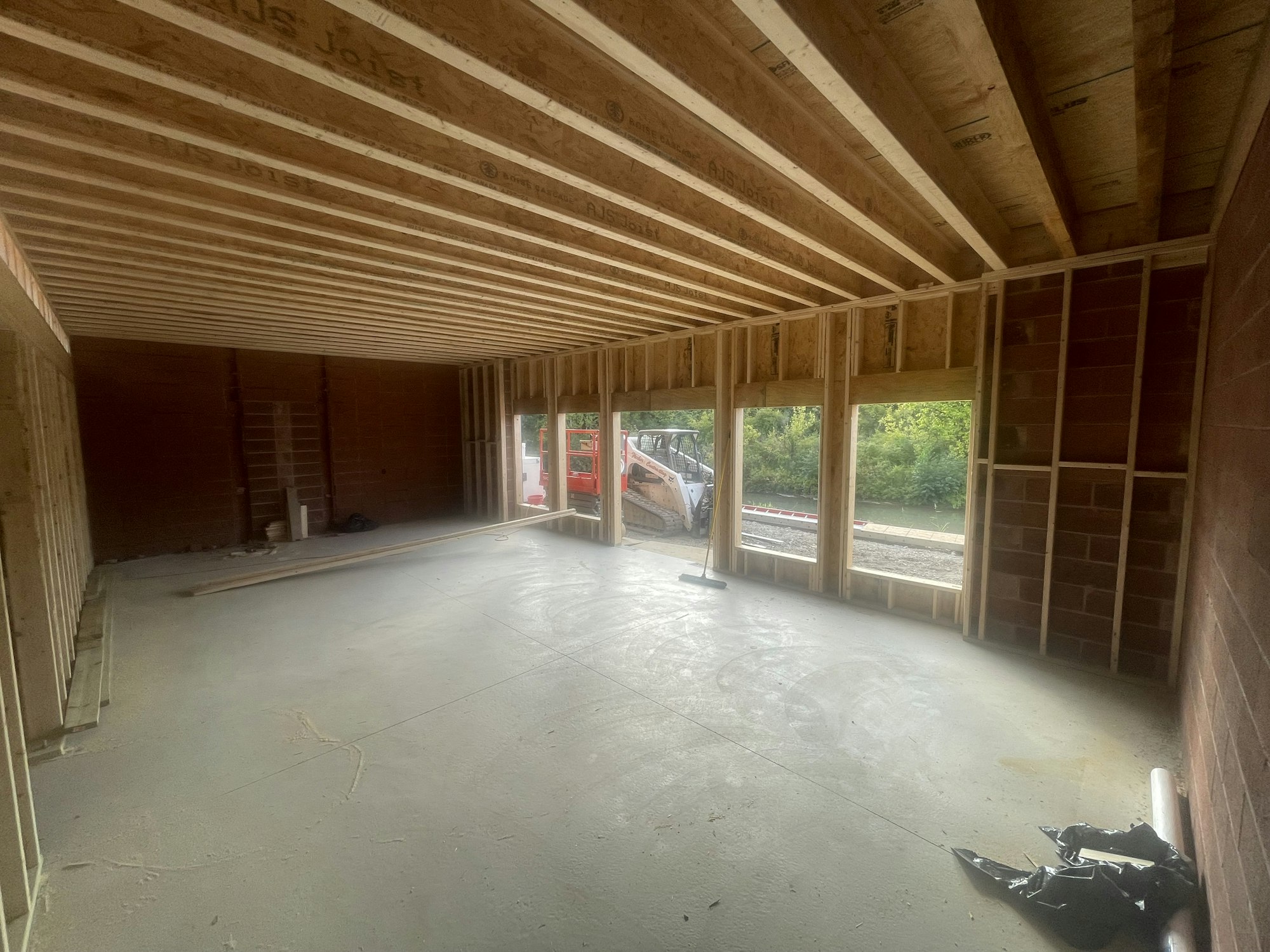 Interior of an unfinished building with exposed wooden beams, large windows, and construction materials.