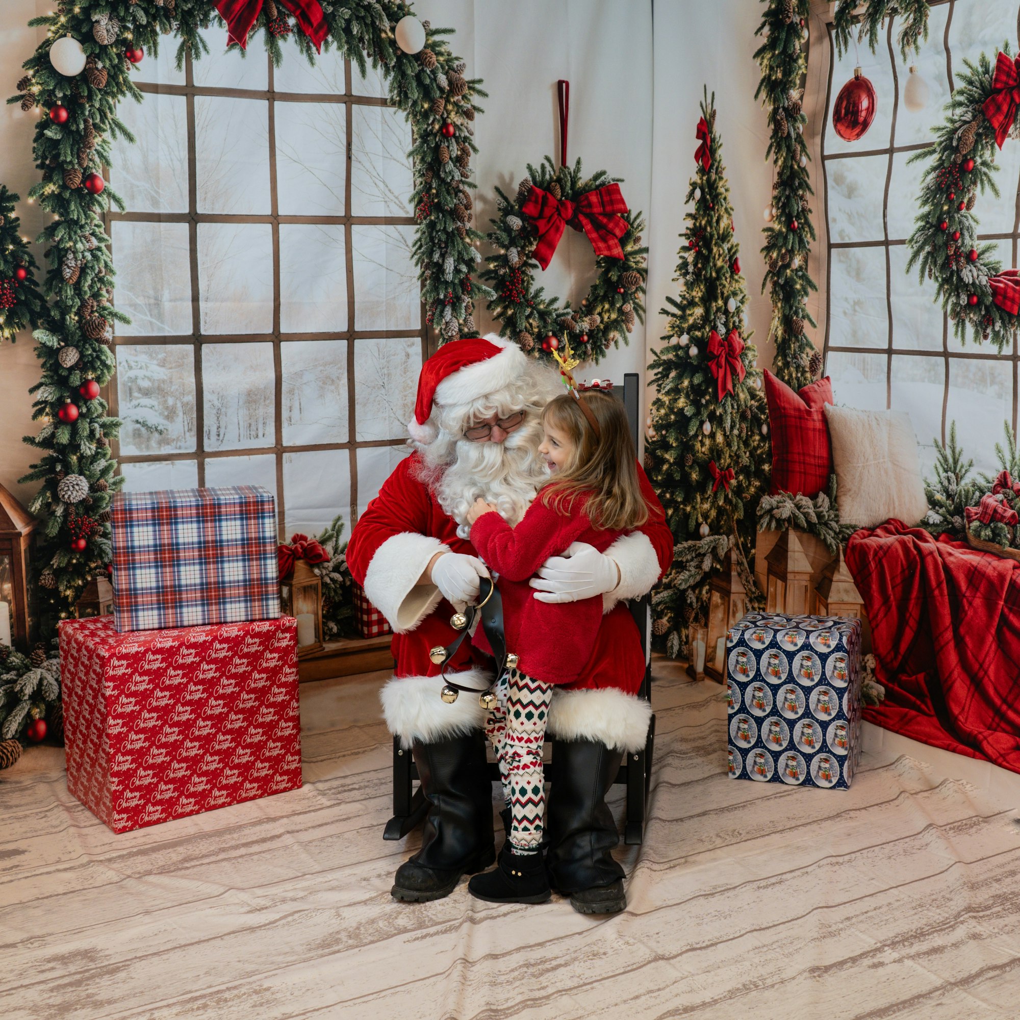 Santa Claus hugging a child in a festive setting with wreaths, Christmas trees, and presents.
