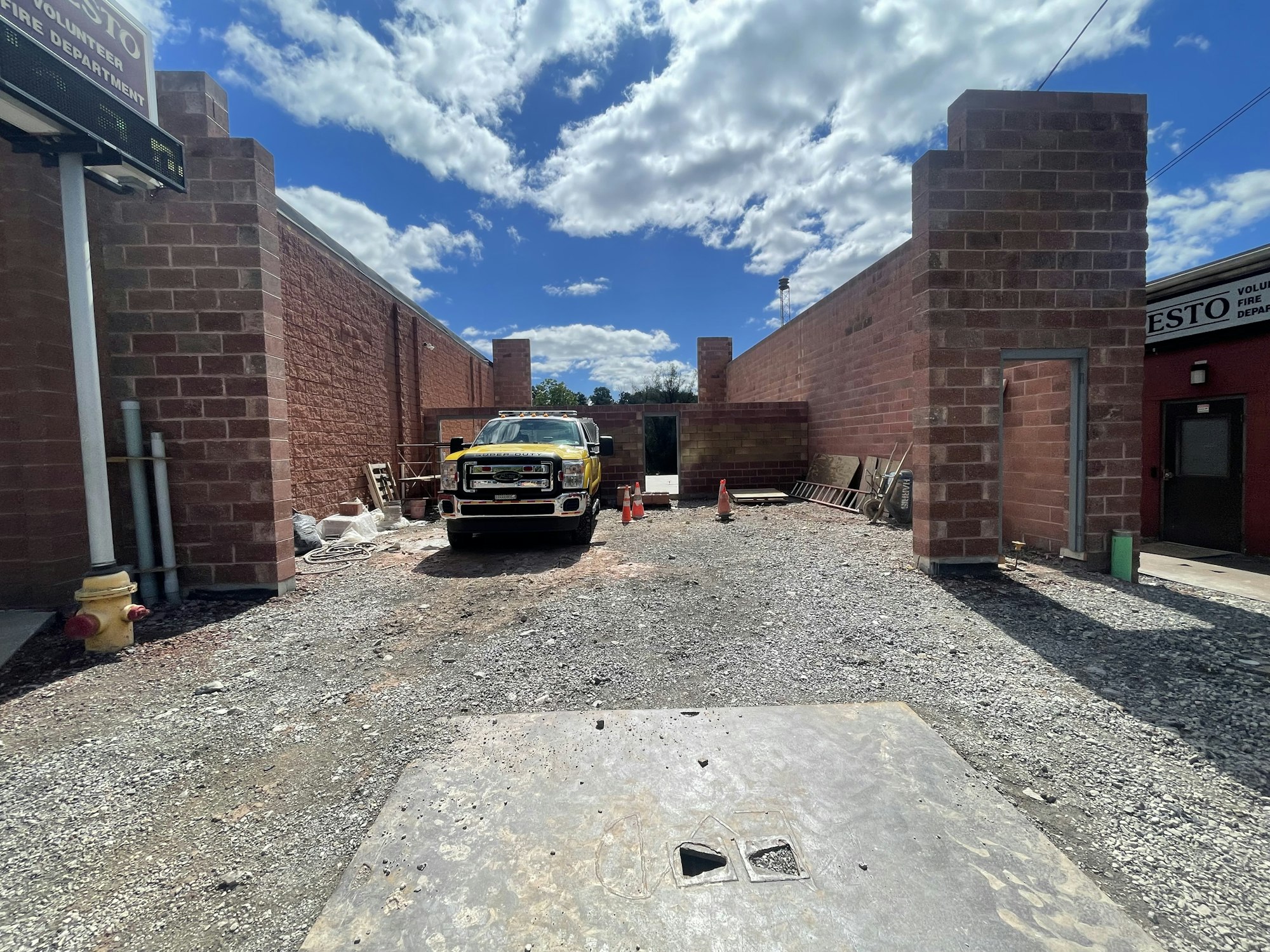A construction site with a yellow truck, gravel ground, brick walls, and a cloudy sky.