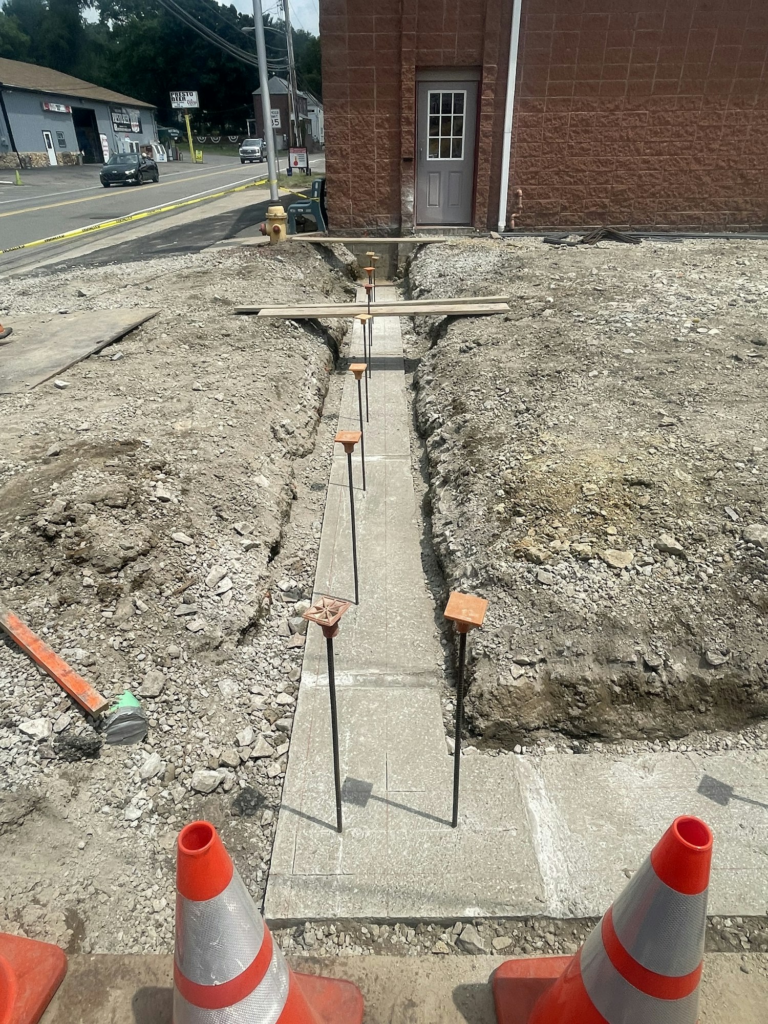 Sidewalk construction with freshly laid concrete slabs, marked by cones and guides for drying, on a sunny day.
