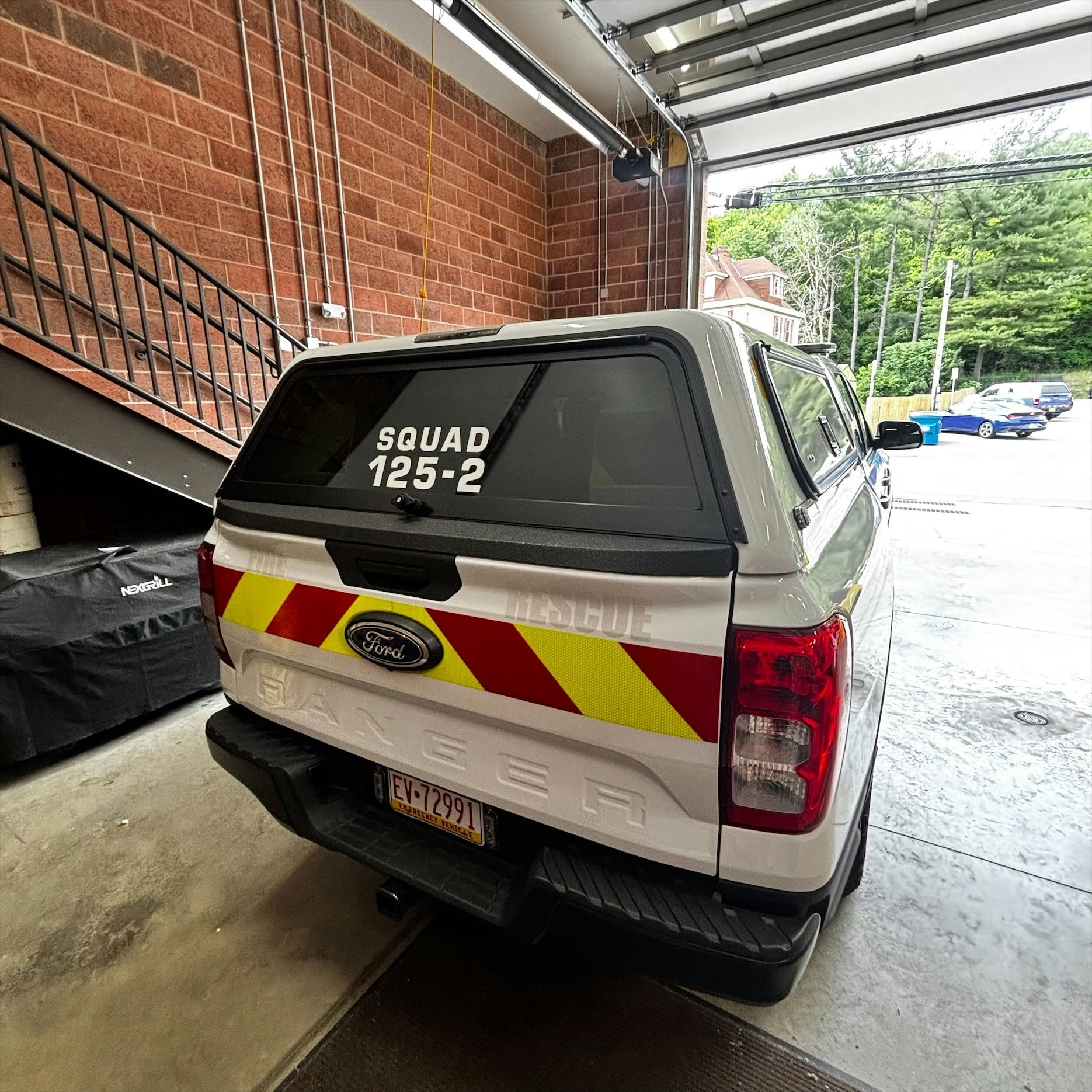 The image shows a Ford Ranger truck labeled "SQUAD 125-2" parked in a garage with a red and yellow reflective design.