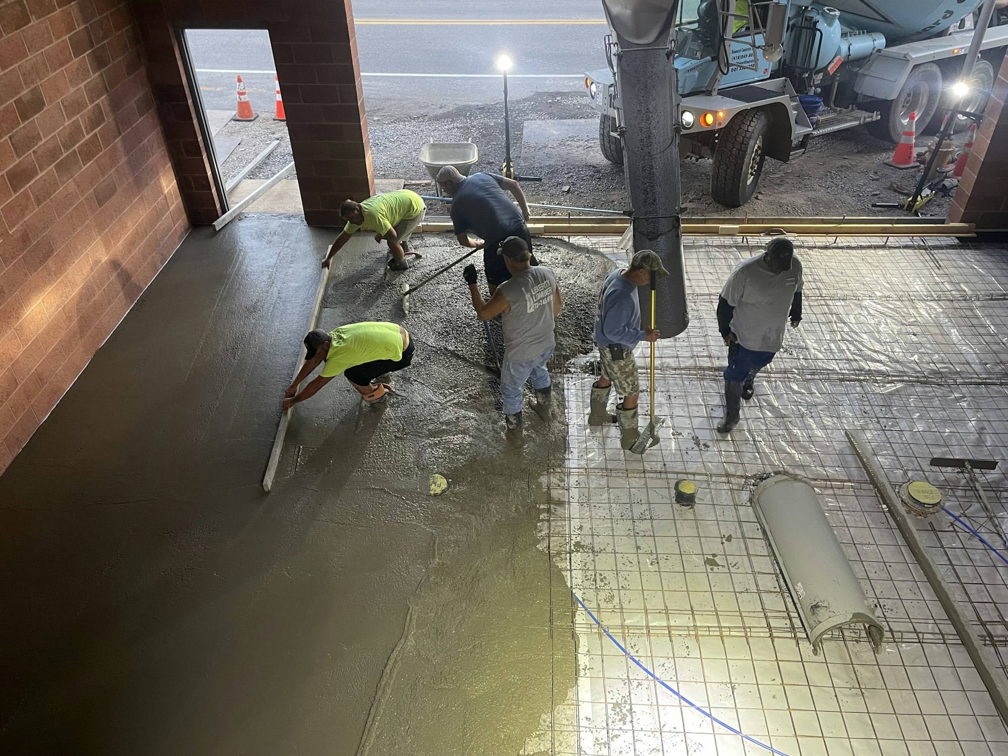 Workers pouring and smoothing concrete with a cement truck in the background.