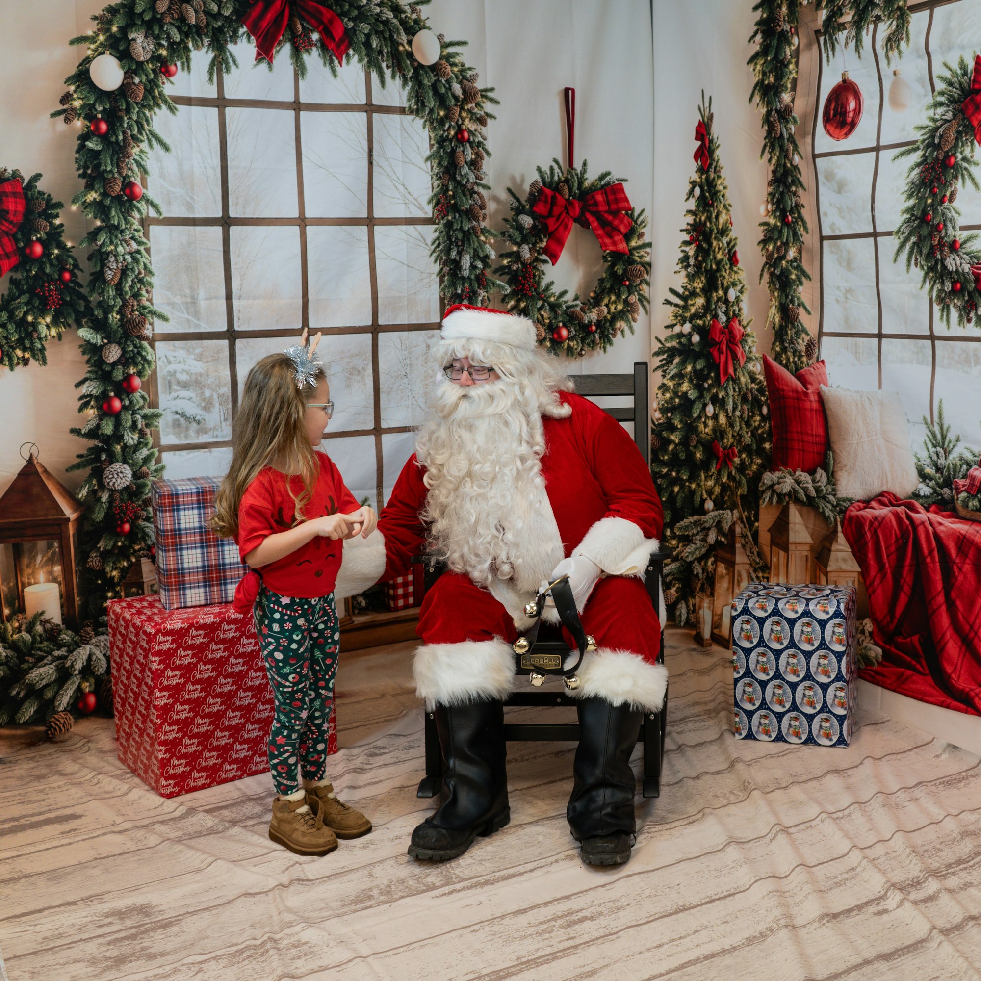 Santa Claus sitting with a child in a Christmas-themed setting, surrounded by wreaths and presents.