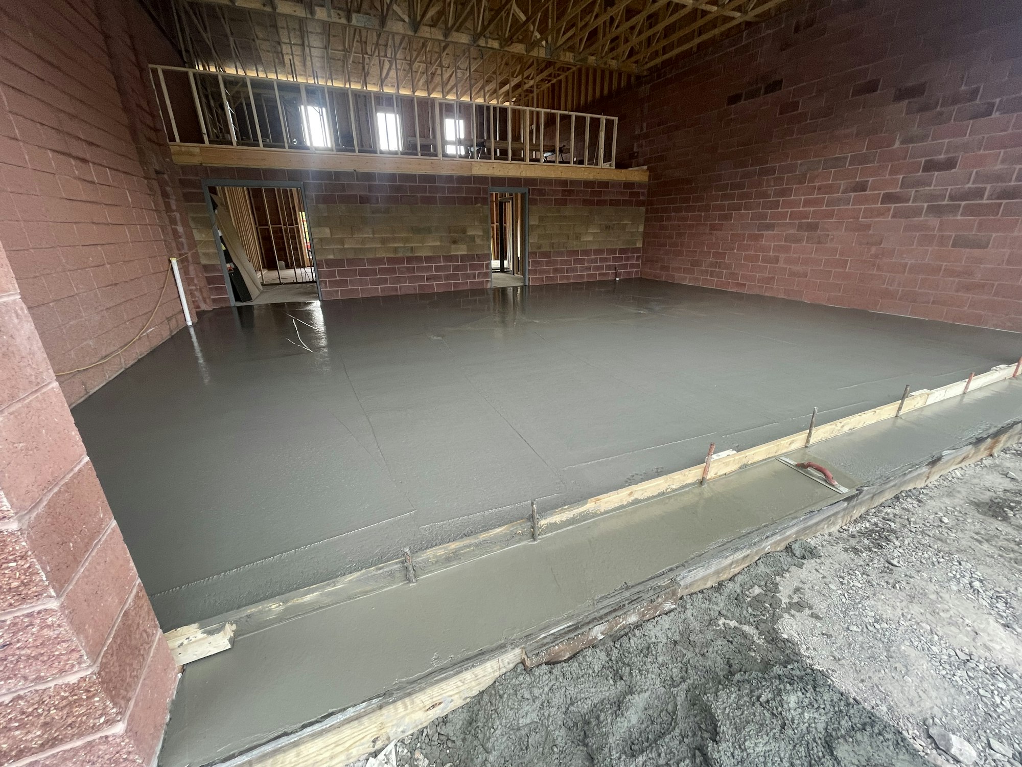 Freshly poured concrete floor in a building under construction with exposed framing and brick walls.