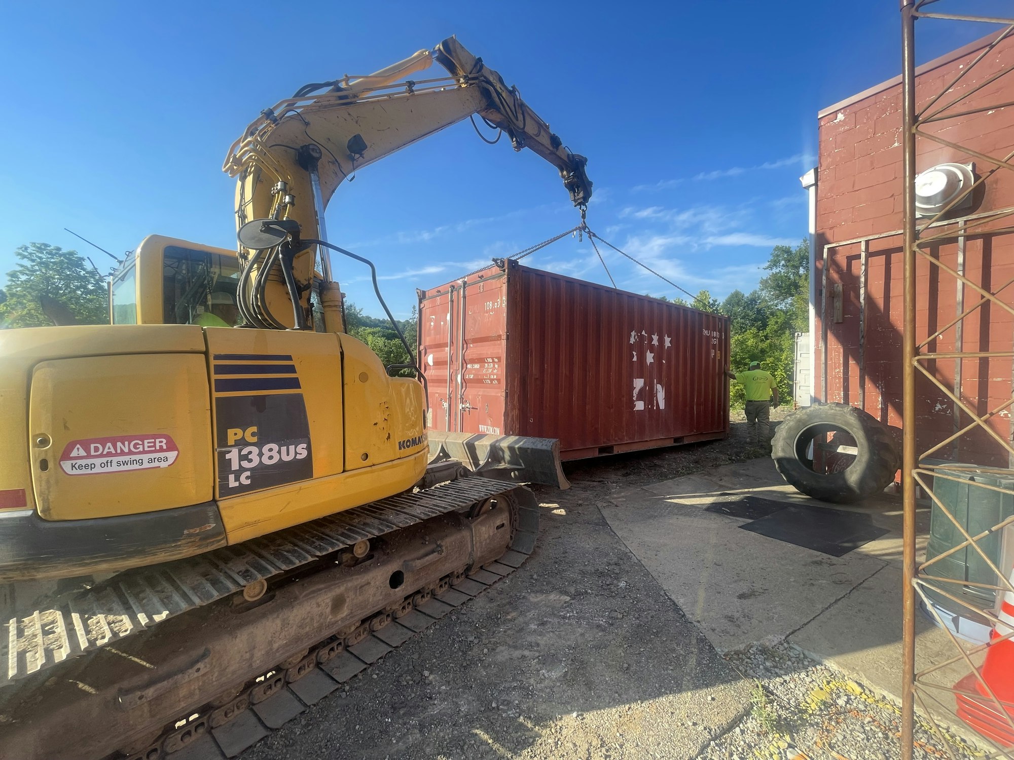 Excavator, shipping containers, and a person in a high-visibility vest at a construction site.