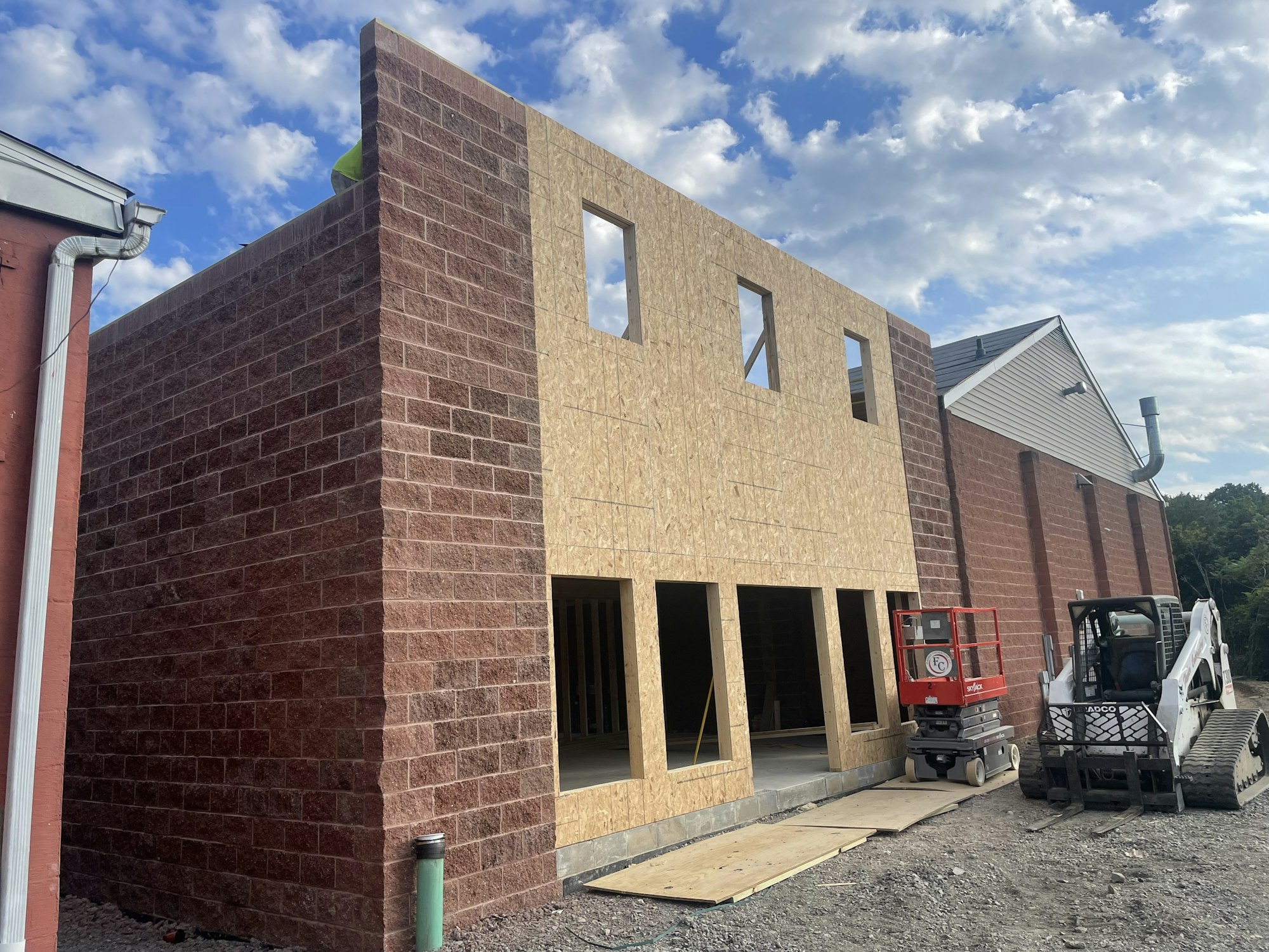 A partially constructed building with exposed plywood and brick facade, alongside construction equipment.