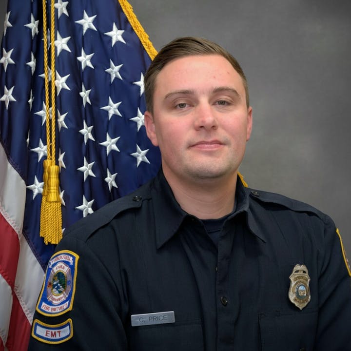 The image shows a man in a black uniform with an EMT badge, posing in front of an American flag.