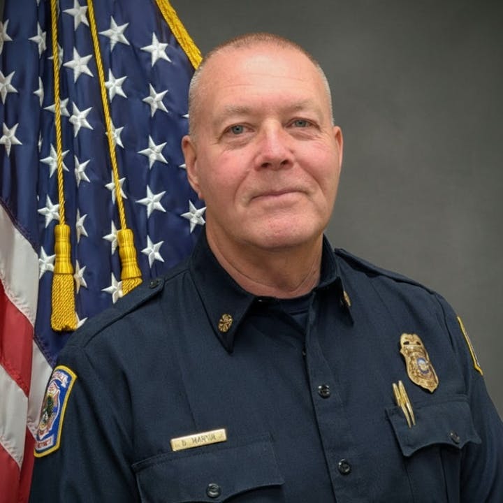g a lawA uniformed individual is posing in front of an American flag, as the Fire Chief.