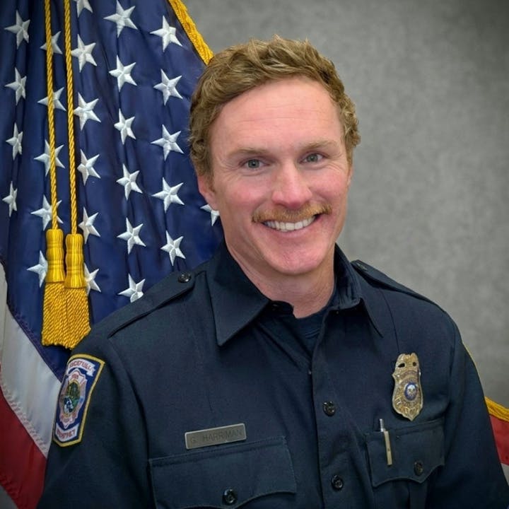 A smiling man in a firefighter uniform standing in front of an American flag.