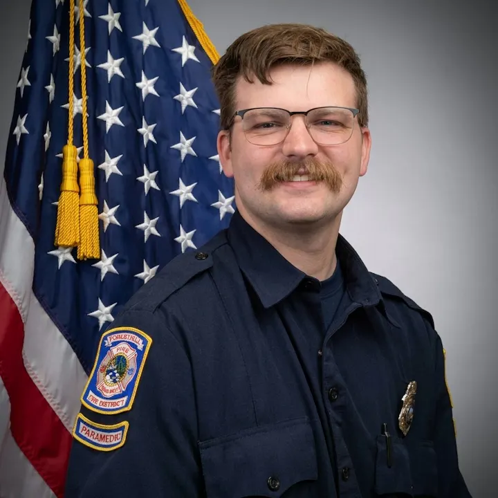 A smiling paramedic in uniform standing in front of an American flag.