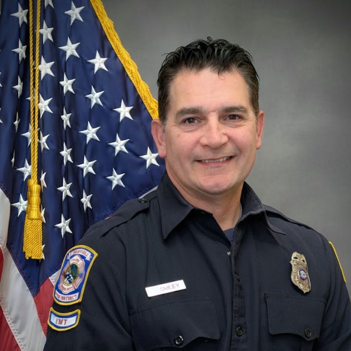 The image features a smiling firefighter in a uniform in front of an American flag backdrop.