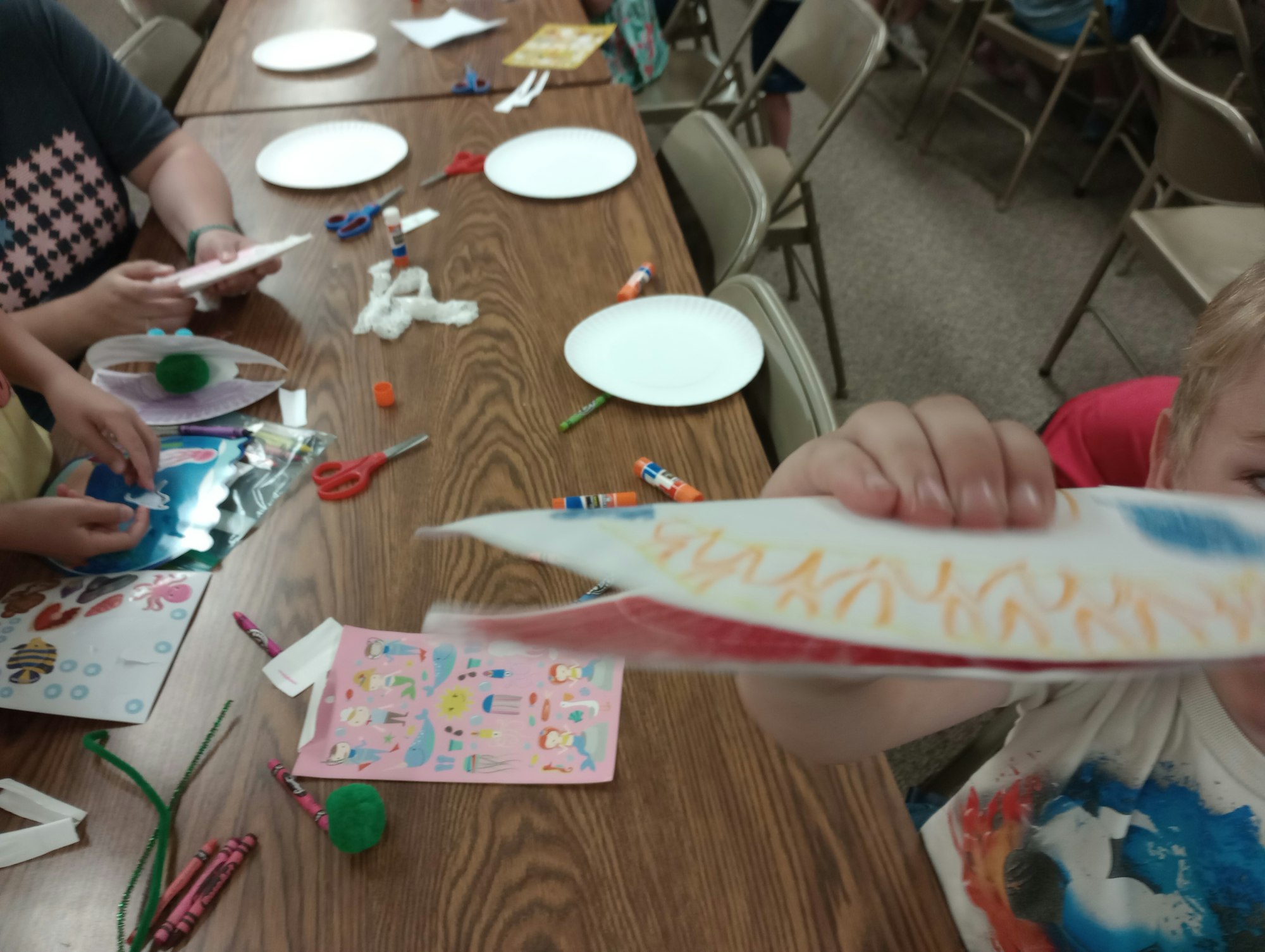 Children doing crafts with paper plates, stickers, and markers at a table.