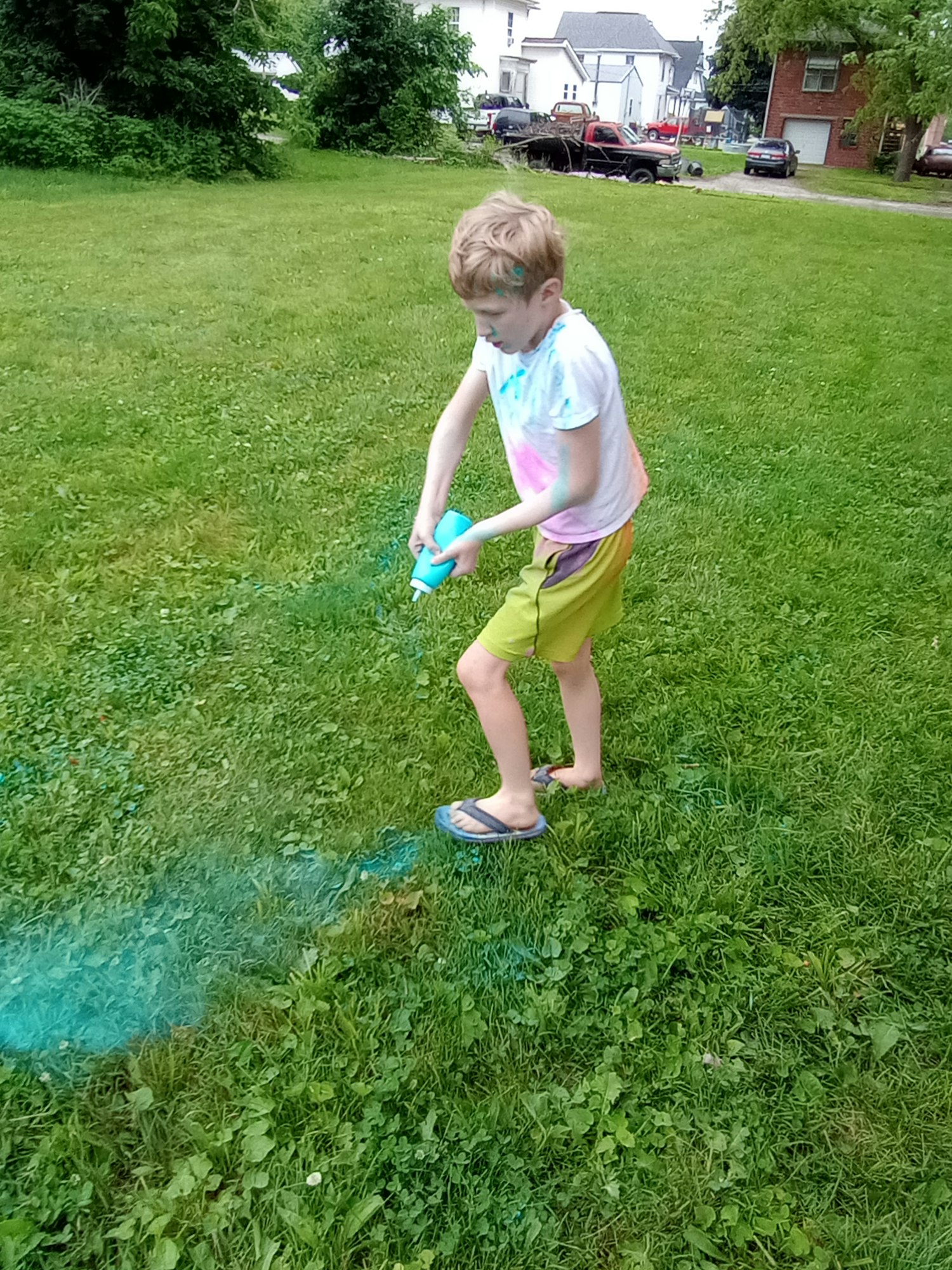 A person in a colorful shirt sprays blue paint on grass in a park.