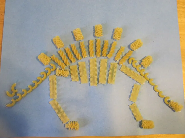 The image features pasta arranged in the shape of a dinosaur on a blue background.