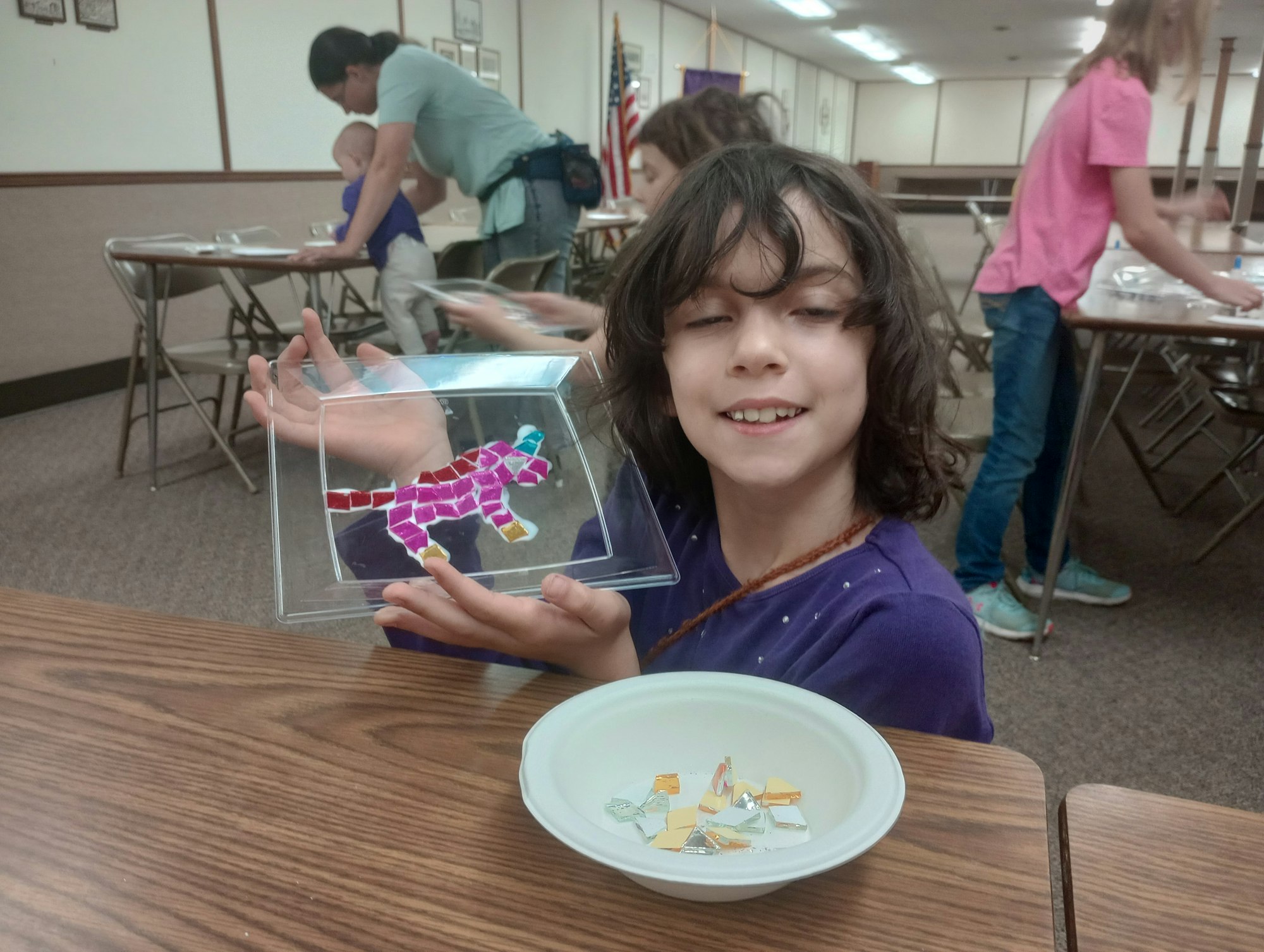 Child showing a colorful mosaic art piece in a classroom.