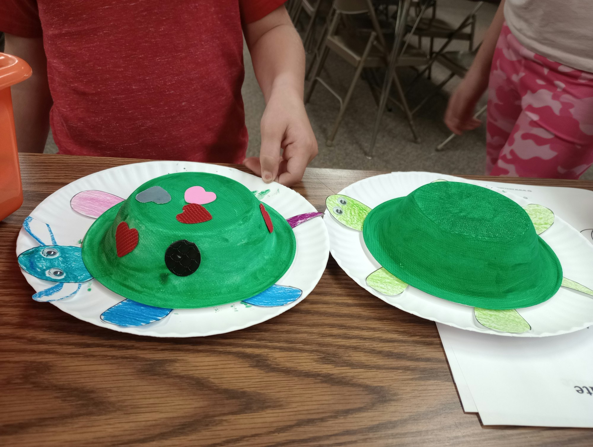 Two paper plate turtle crafts painted green, decorated with hearts.
