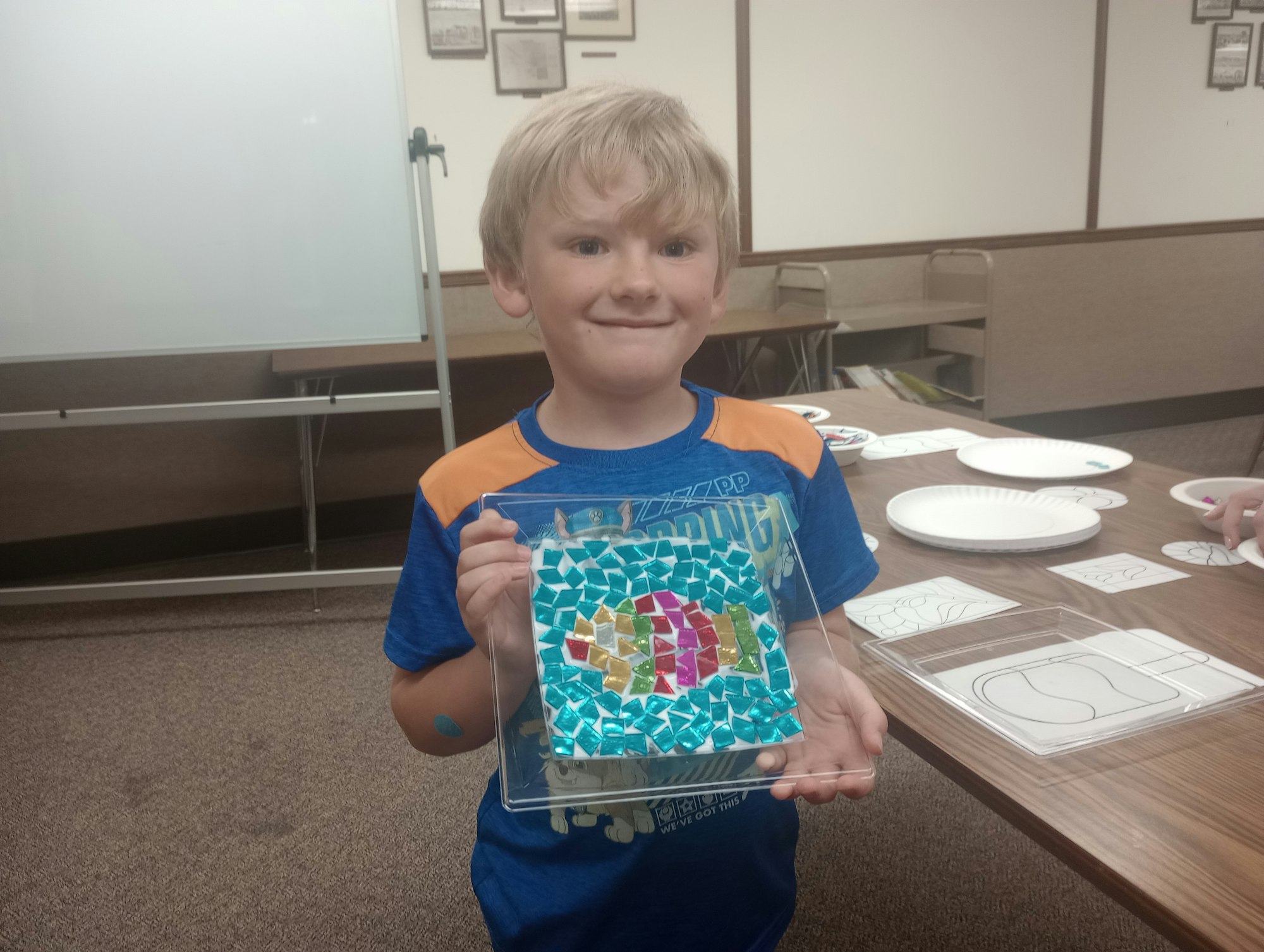 A child holding a colorful mosaic art piece in a classroom setting.