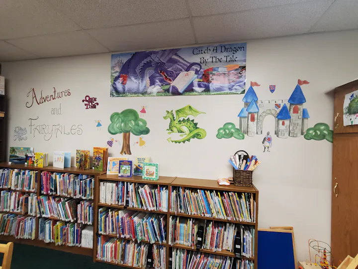 A vibrant library wall featuring fairy tale themes, including a dragon, castle, and colorful bookshelves filled with children's books.