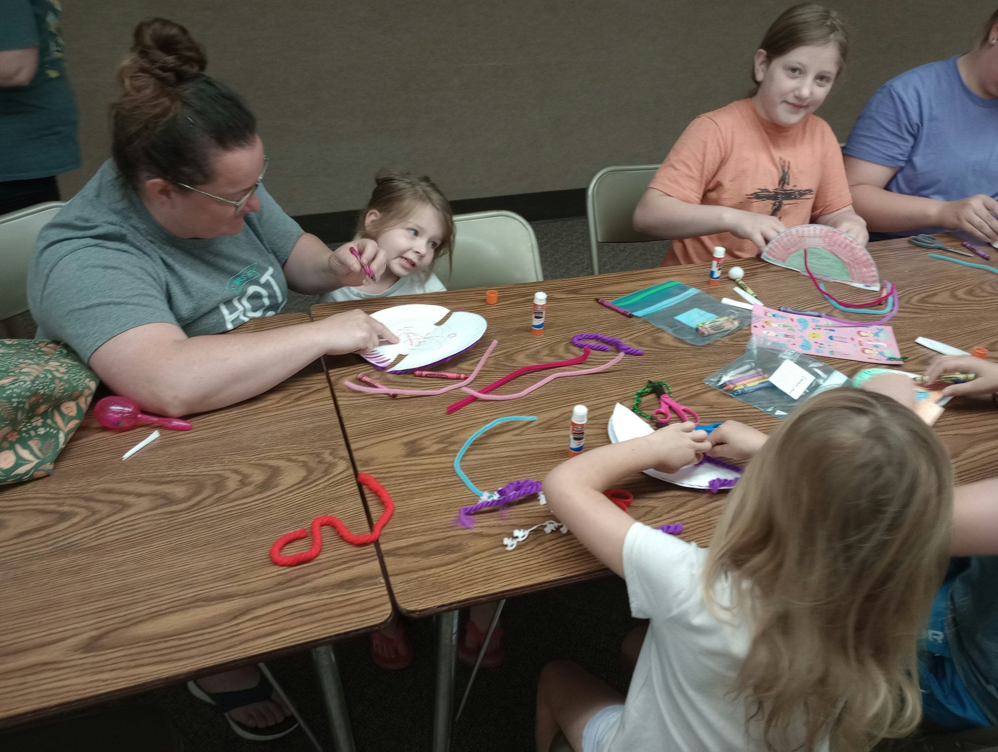 People at a table doing crafts with paper plates, pipe cleaners, and glue sticks.