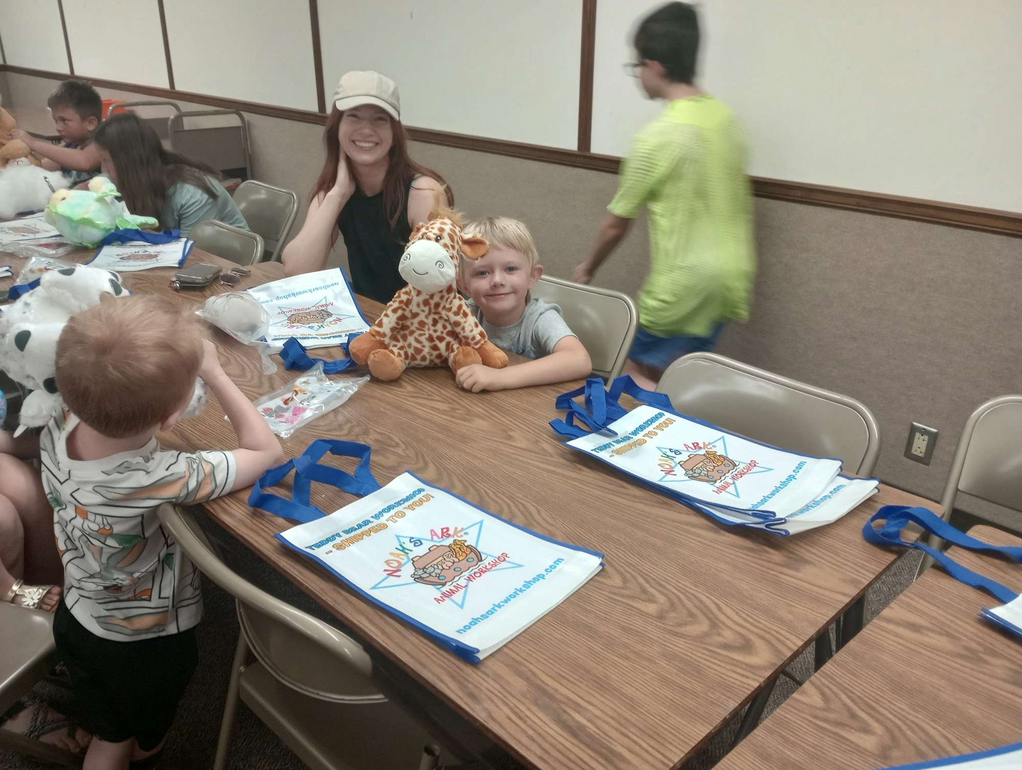 People at a table with stuffed animals and activity bags, smiling.