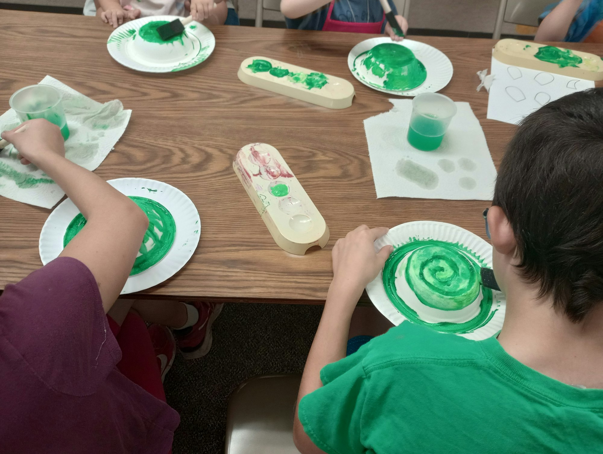 Children painting paper plates green at a table with brushes and paint.